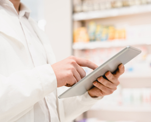 gestão de estoque de itens consignados- Imagem de uma pessoa mexendo no tablet e ao fundo um estoque de farmácia ou hospital