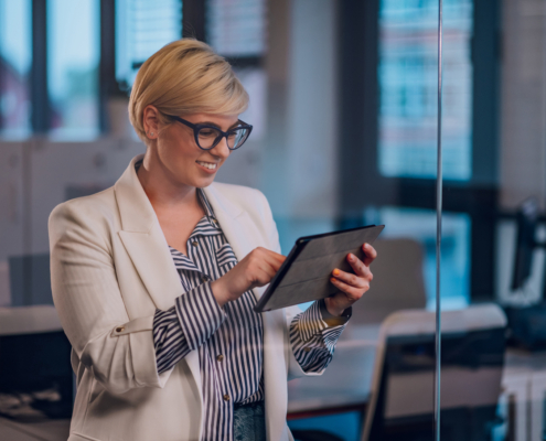 Imagem de mulher de negócios no trabalho com expressão confiante como usando um tablet digital no escritório. Vista através de uma parede de vidro.