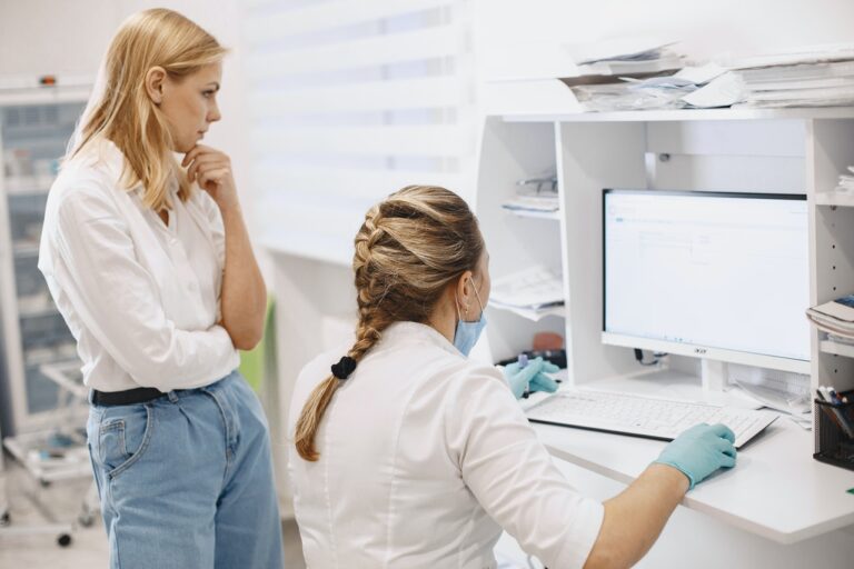 Imagem de duas mulheres olhando na tela de um computador. Um delas está em pé e a outra sentada.