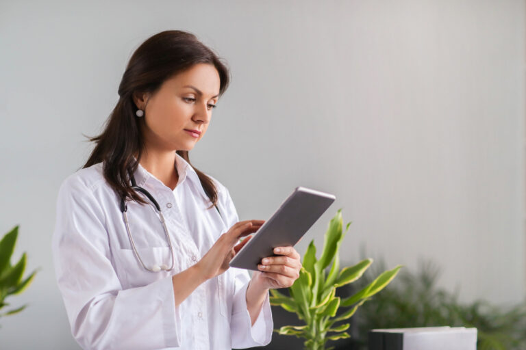 Imagem de uma mulher vestida com um jaleco, segurando e olhando um tablet