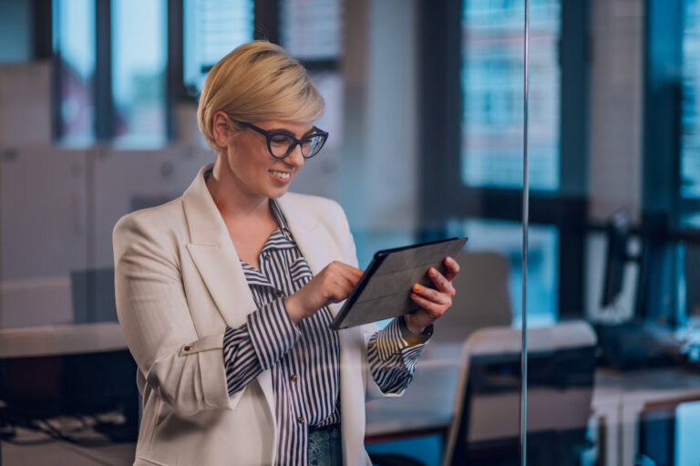 Imagem de mulher de negócios no trabalho com expressão confiante como usando um tablet digital no escritório. Vista através de uma parede de vidro.